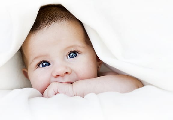 Blue eyed baby laying under white towel