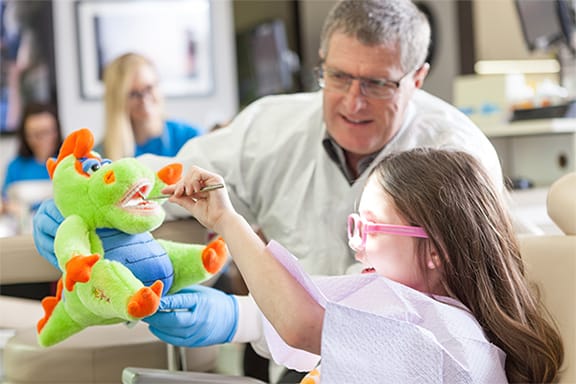 Dentist using stuffed dinosaur with teeth to show child dental tools
