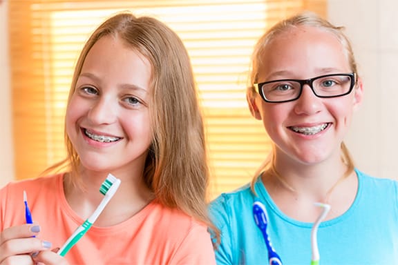 Two teen girls with braces smiling and holding tooth brushes